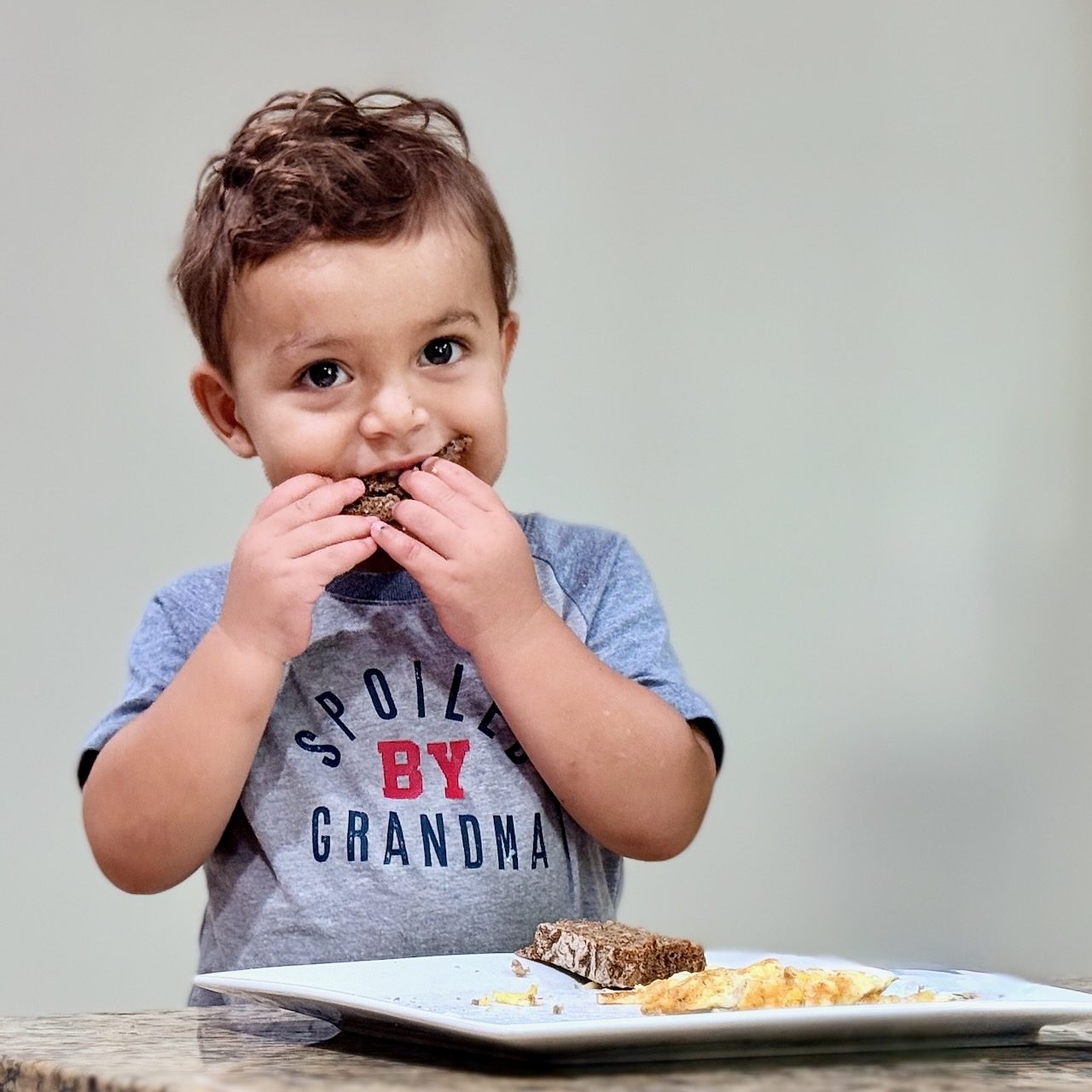 A toddler eating a slice of Lagomberry rye sourdough with eggs