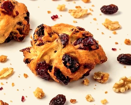 A pastry bite packed with raisins, pecans and walnuts scattered beside it