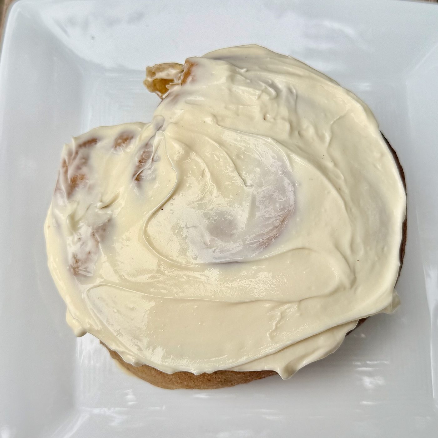 A sourdough pumpkin cinnamon roll under a thick layer of cream cheese frosting
