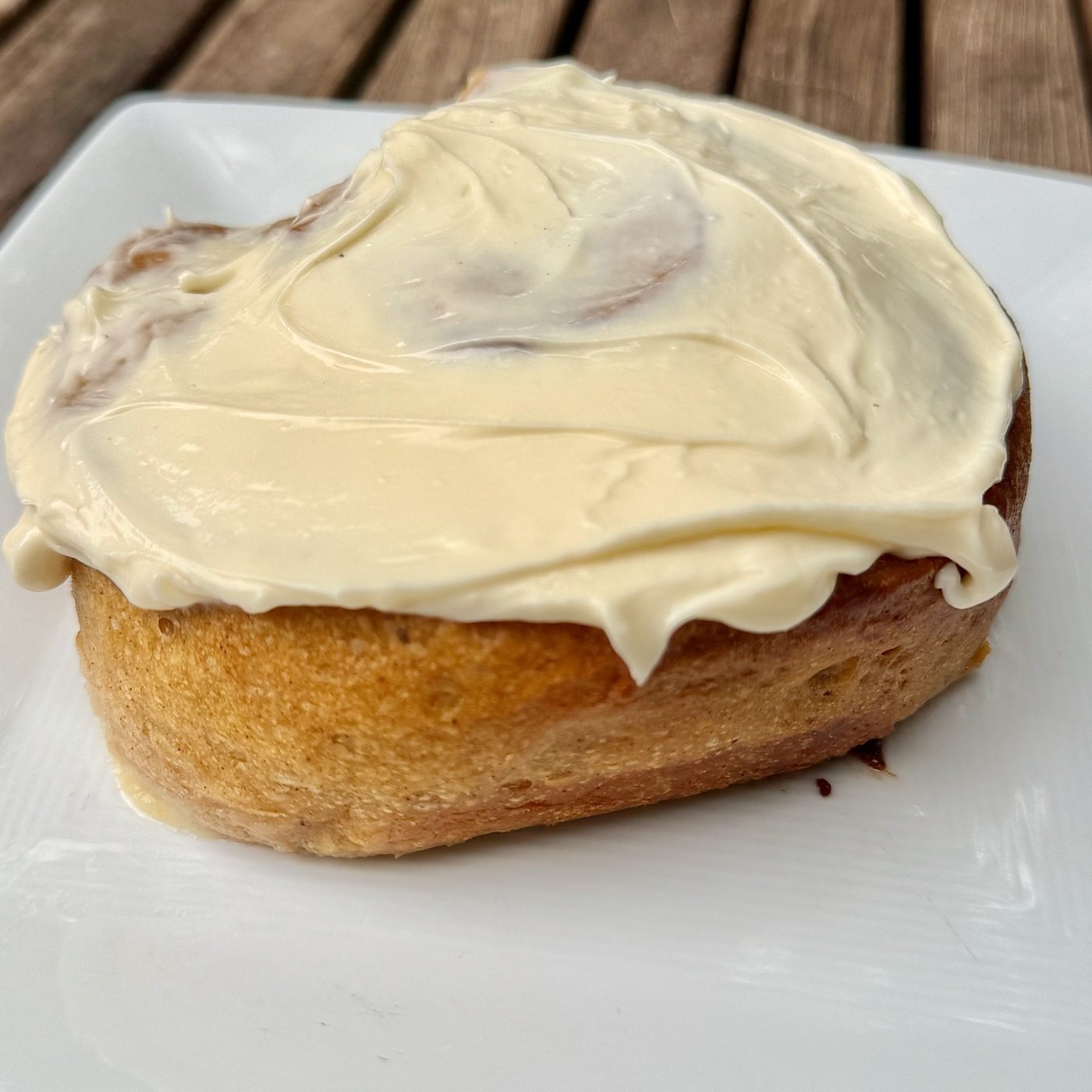 A pumpkin cinnamon roll from the side, golden crust under the frosting