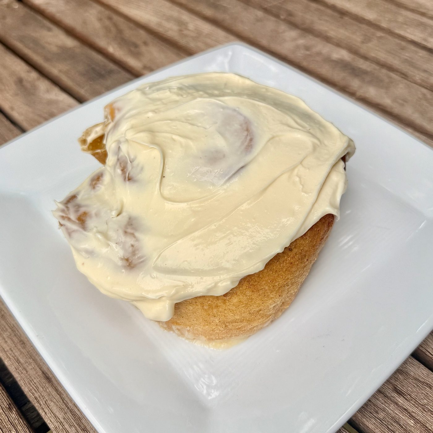 A pumpkin cinnamon roll on a white plate, frosting spread edge to edge