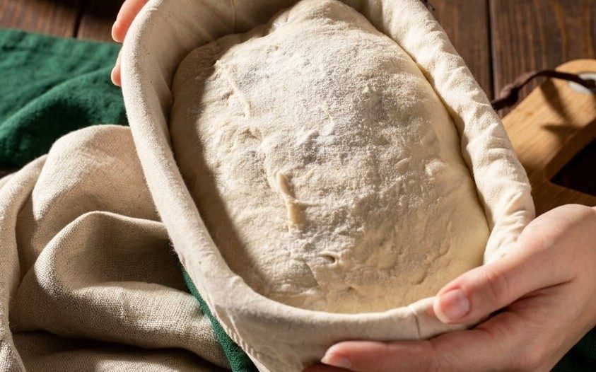 Hands lifting dough from a proofing basket