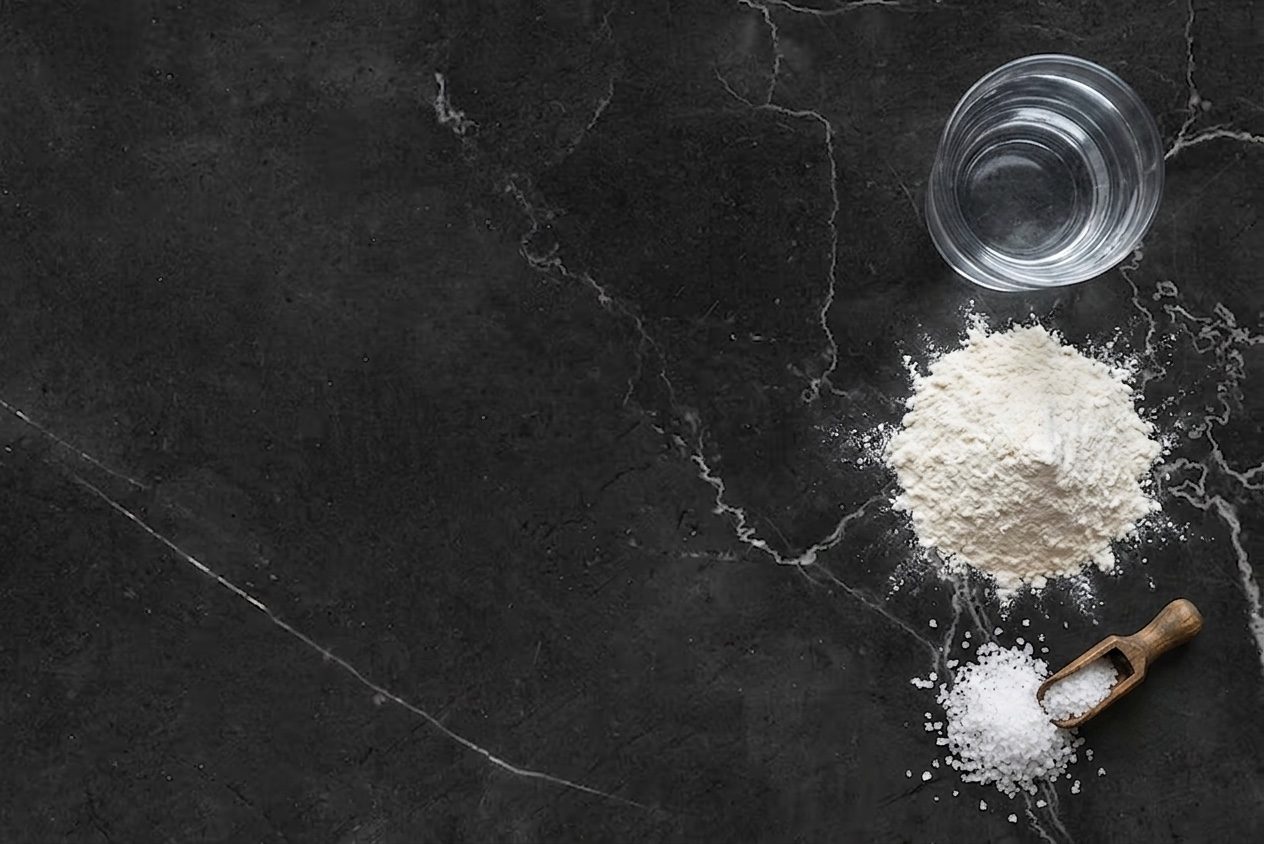 Water, stone-ground flour and coarse sea salt laid out on dark stone