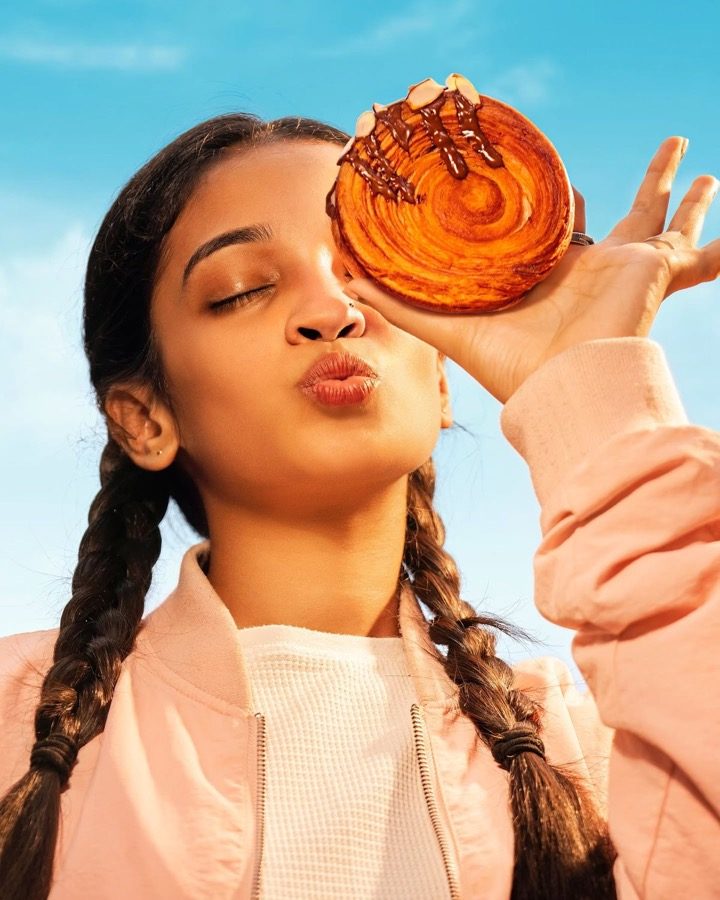 A girl holding a big glazed pastry up to her face
